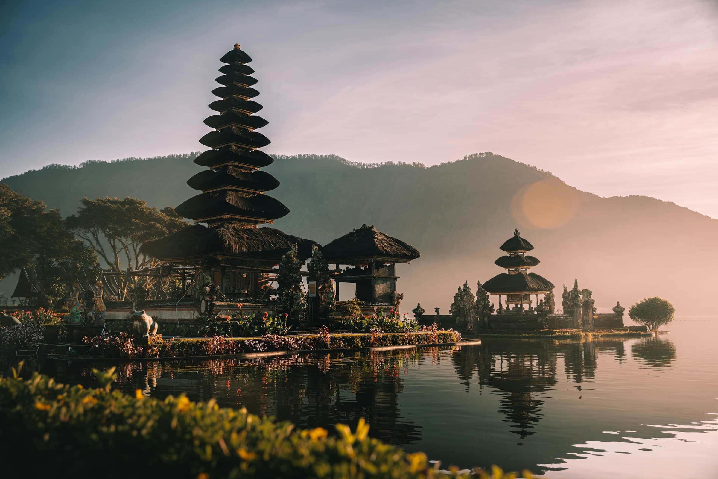 Balinese lakeside temple at sunrise with mountains behind it